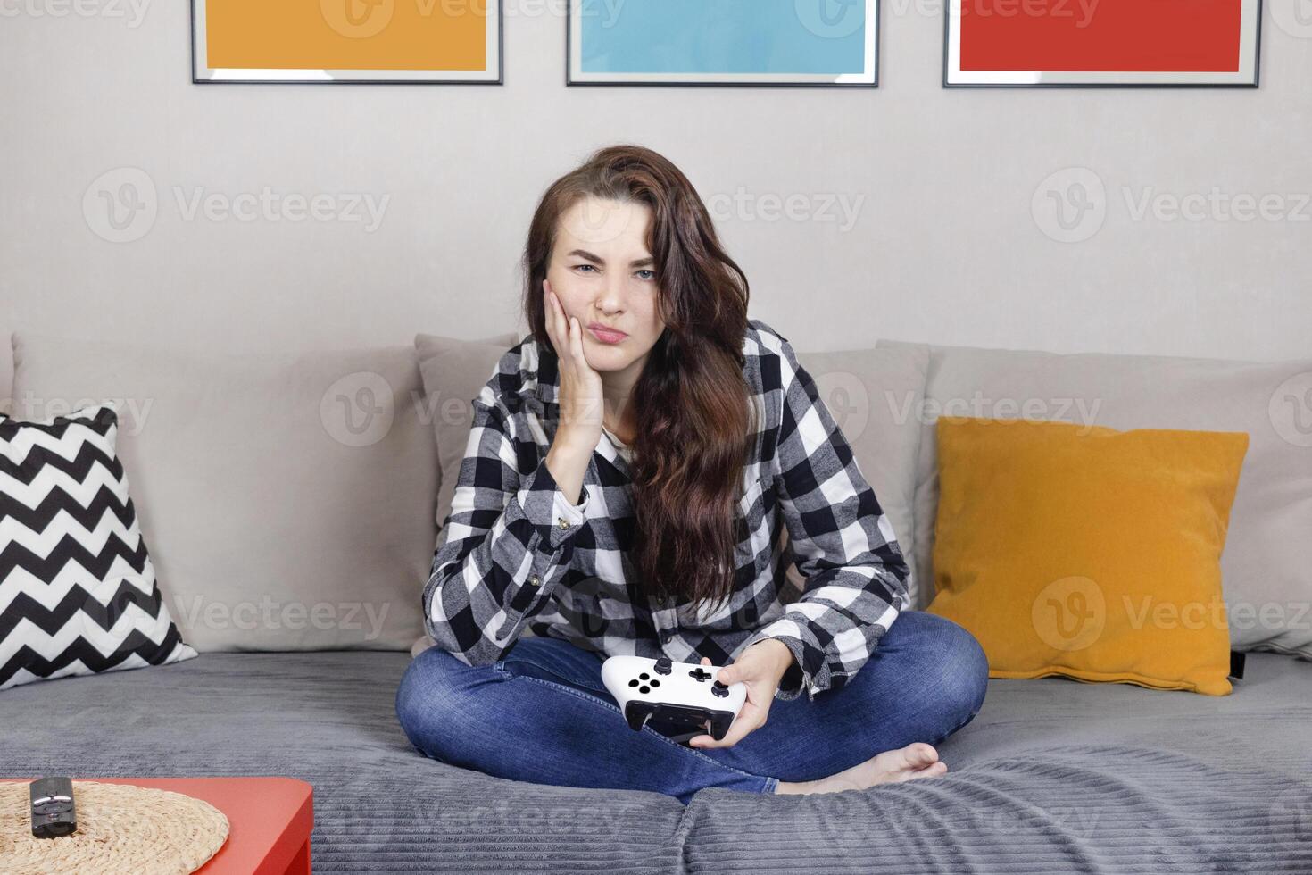 Brunette woman is holding a white joystick. She plays game on the console. Woman bored, uninteresting to play vgames, bored stay at home photo