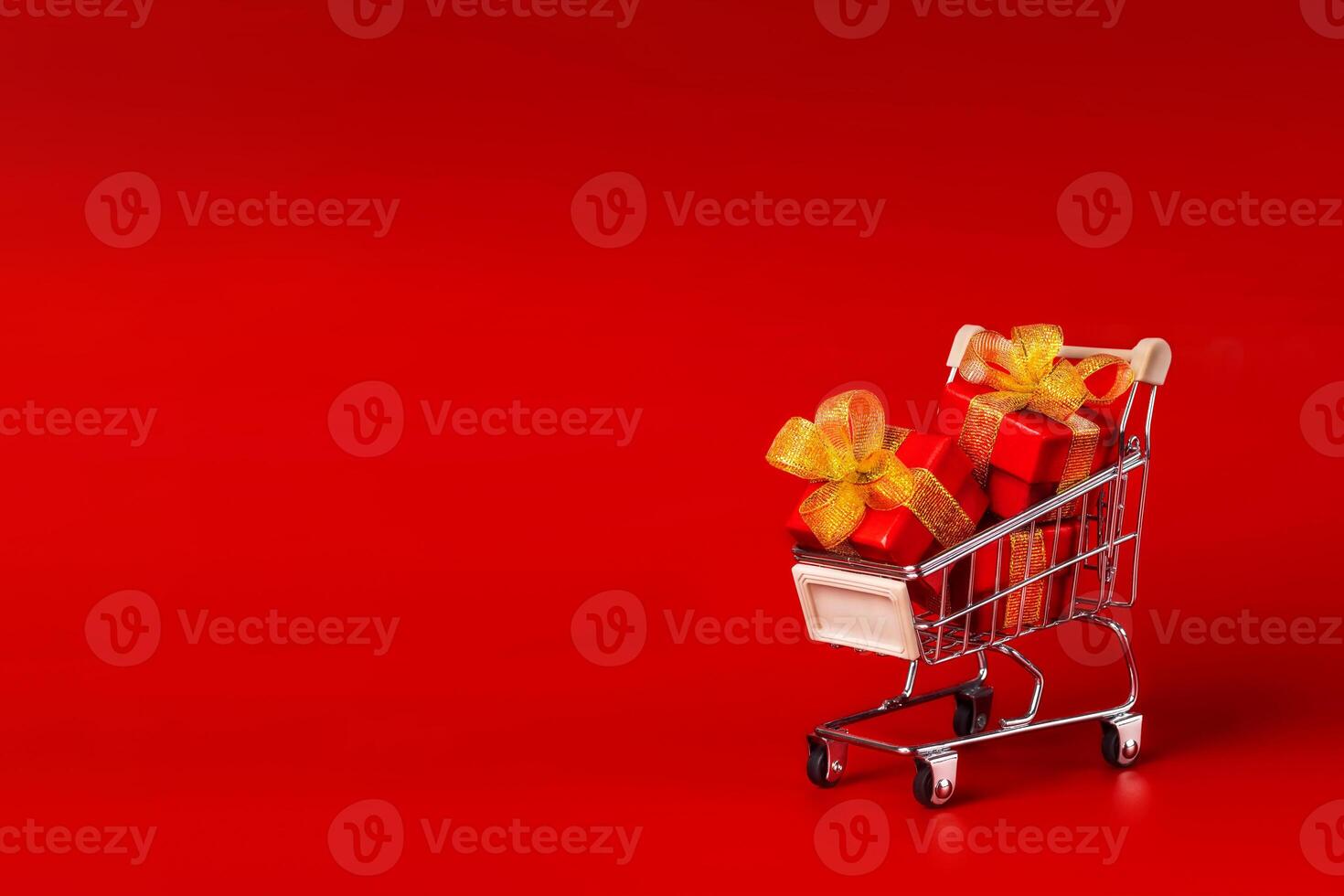 red boxes with gold bows on supermarket trolley. Discounts, Black Friday, Christmas, Birthday, New Year. Red background, Copy space photo