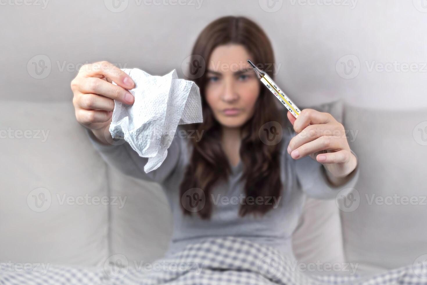 Concept of disease, home treatment. A woman caught a cold, holds a thermometer and napkins for a runny nose photo