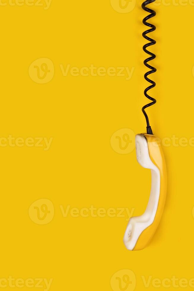 Yellow old phone handset dangles on wire. yellow background vertical banner poster copy space photo