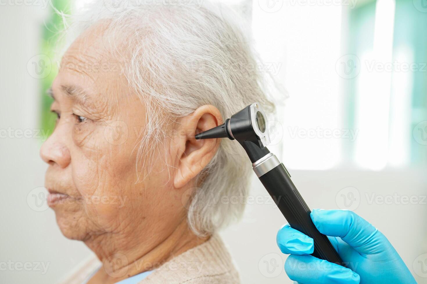 Audiologist use otoscope checking ear of elderly woman patient treating hearing loss problem. photo