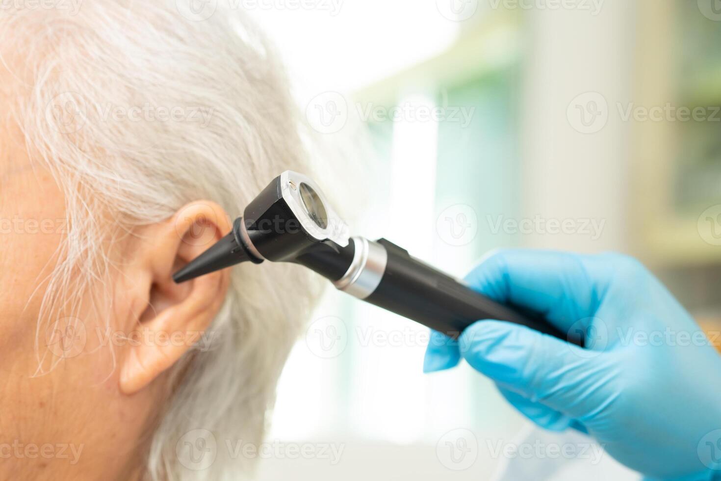 Audiologist use otoscope checking ear of elderly woman patient treating hearing loss problem. photo