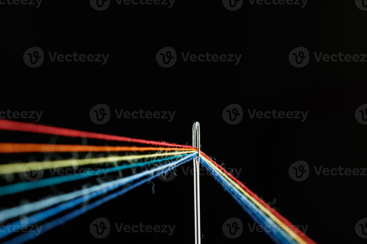 multi-colored threads for sewing in the form of a rainbow pass through an antique needle on a black background photo