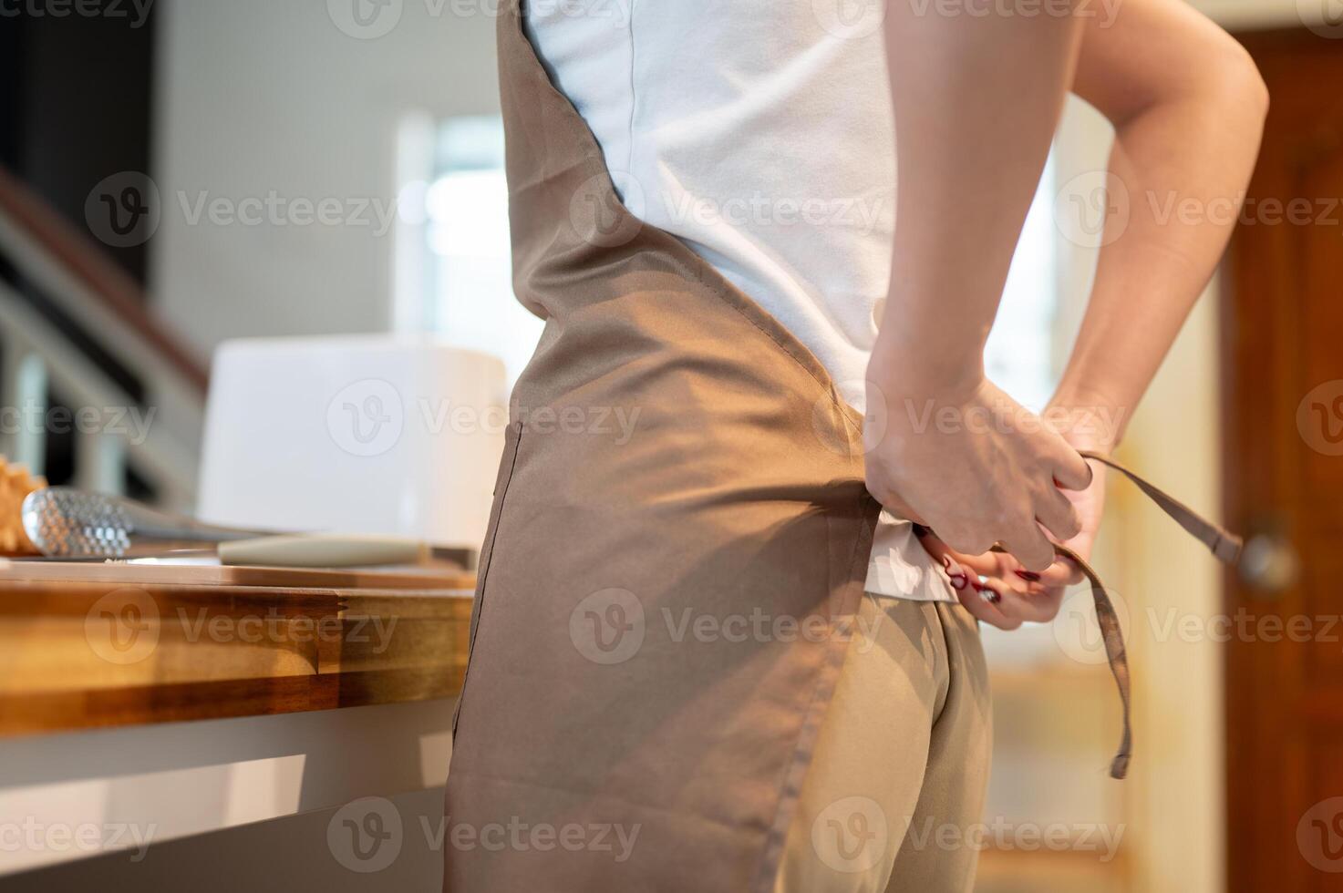 A close-up of a woman wearing an apron, standing beside a kitchen table in the kitchen. photo