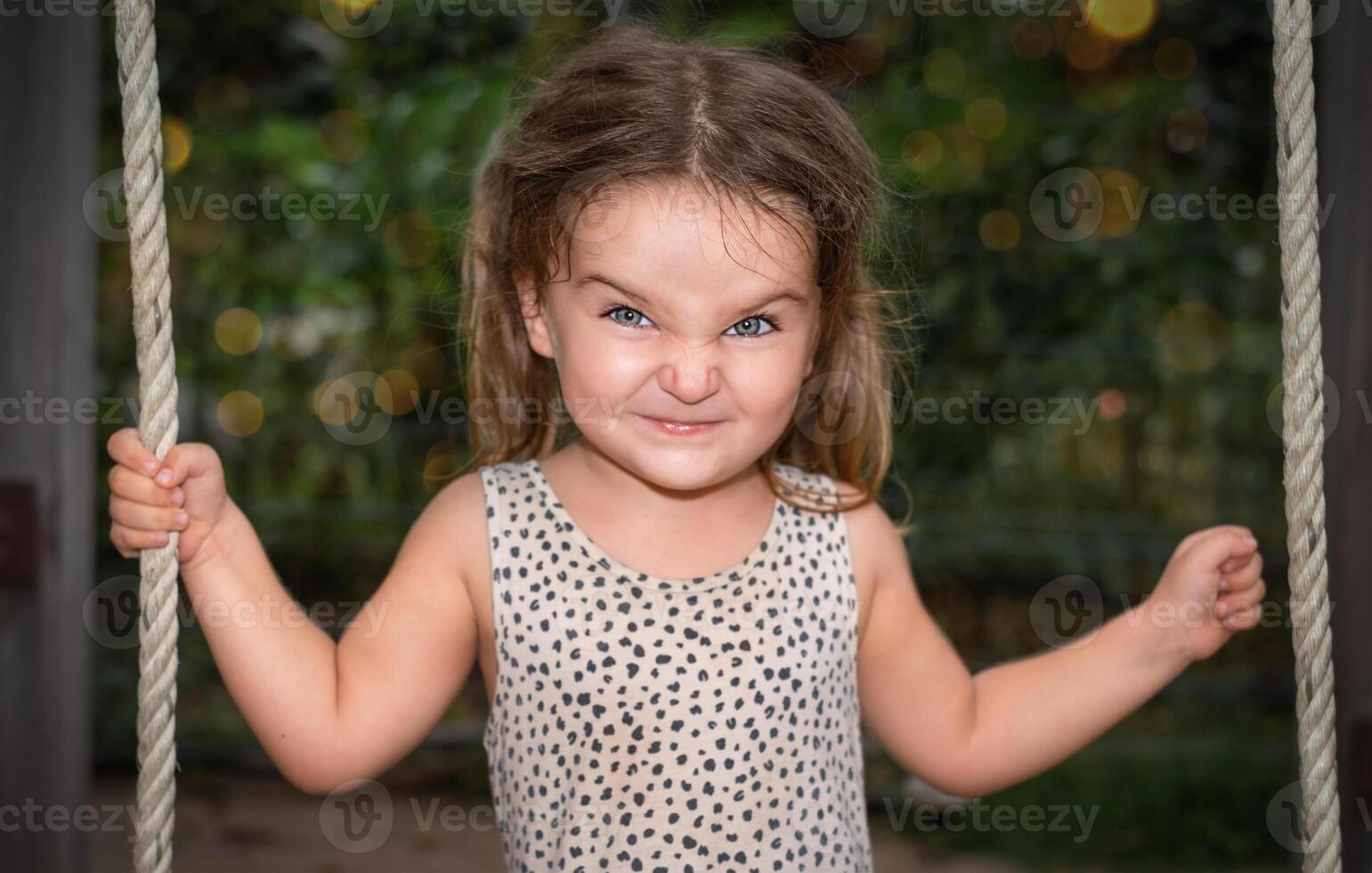 Portrait of a child girl with grimacing on a swing photo