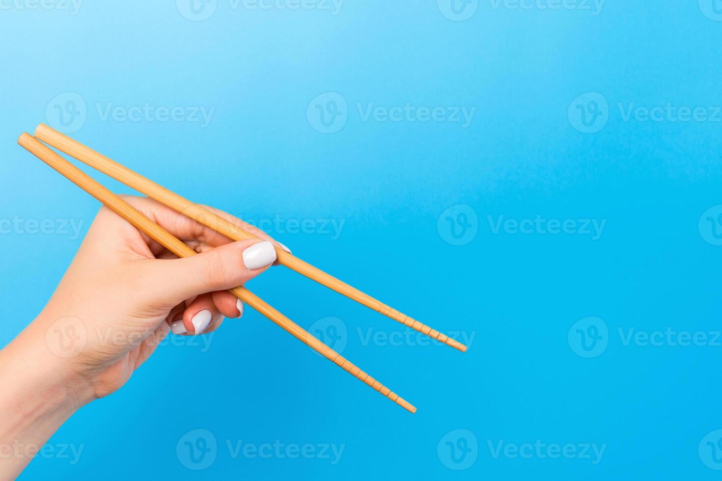 Female hand with chopsticks on blue background. Traditional asian food with emty space for your design photo