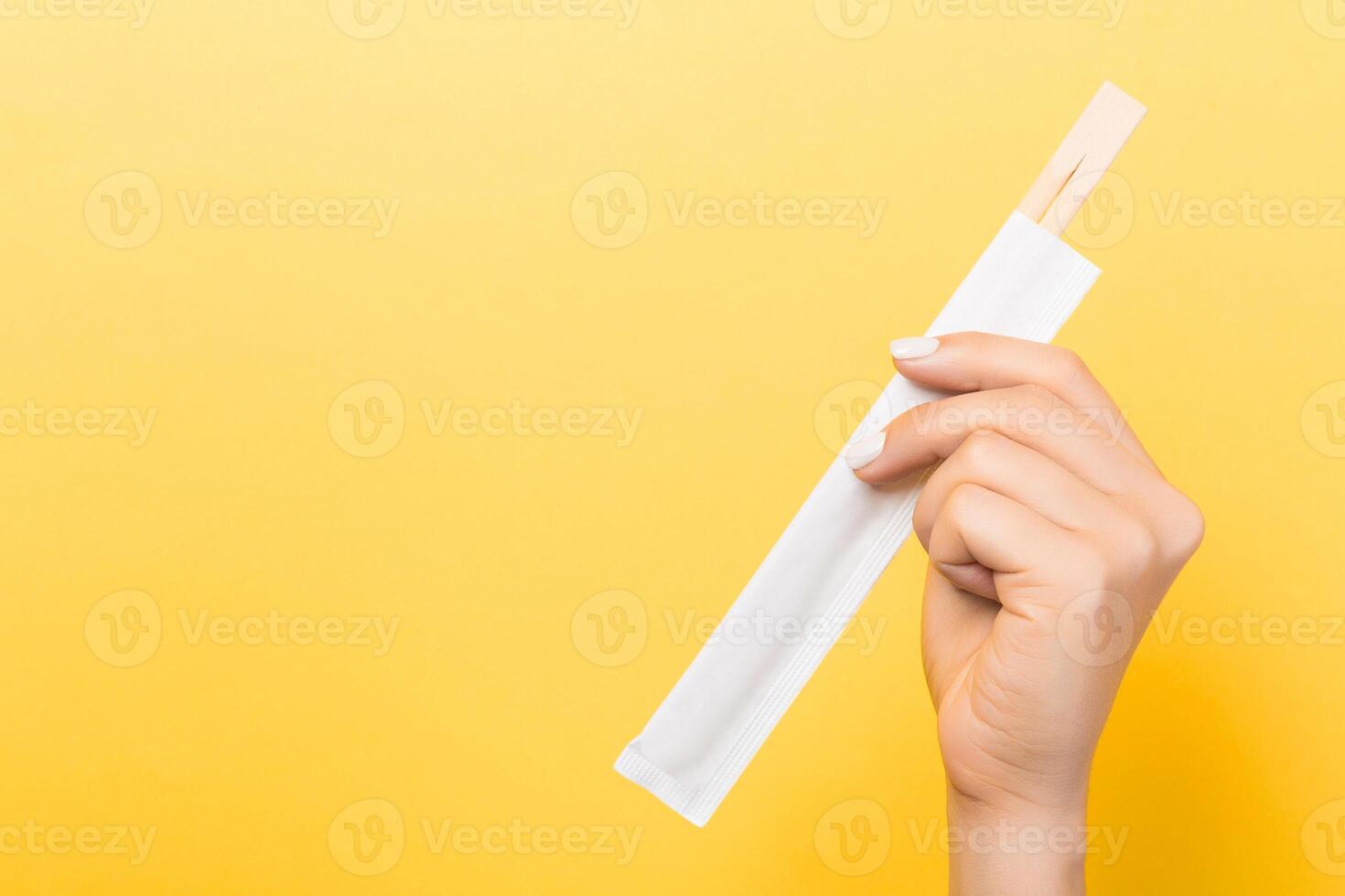 Woman's hand holding chopsticks in a pack on yellow background. Chinese food concept with empty space for your design photo
