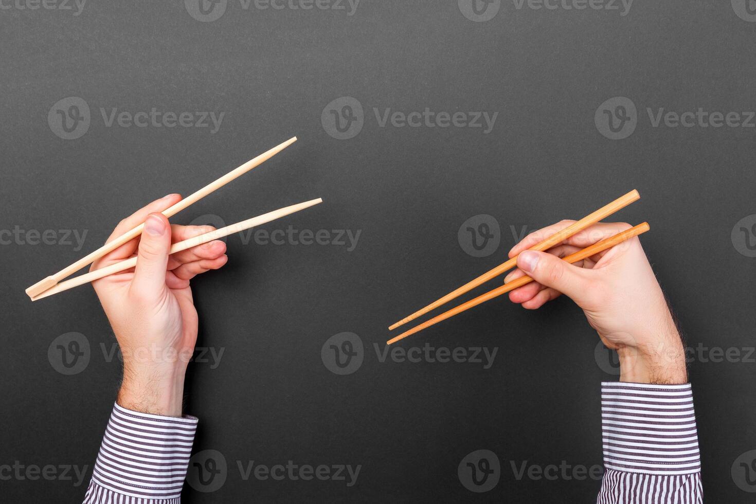 Creative image of wooden chopsticks in two male hands on black background. Japanese and chinese food with copy space photo