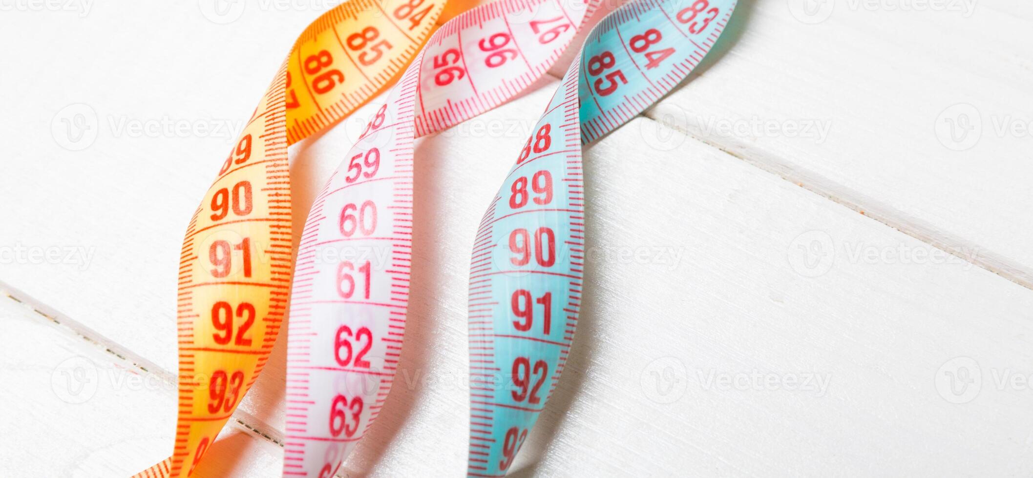 Close up of colorful measure tapes on wooden background. Perfect female figure measurements concept photo