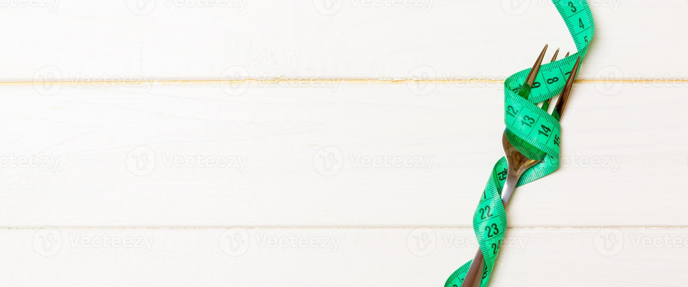 Top view of obesity concept with fork wrapped in measuring tape on wooden background with space for your creative ideas photo