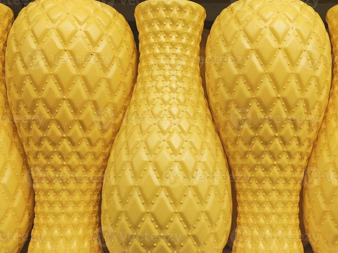 A collection of yellow decorative vases with diamond-textured patterns arranged in a row, creating a symmetrical and vibrant display photo
