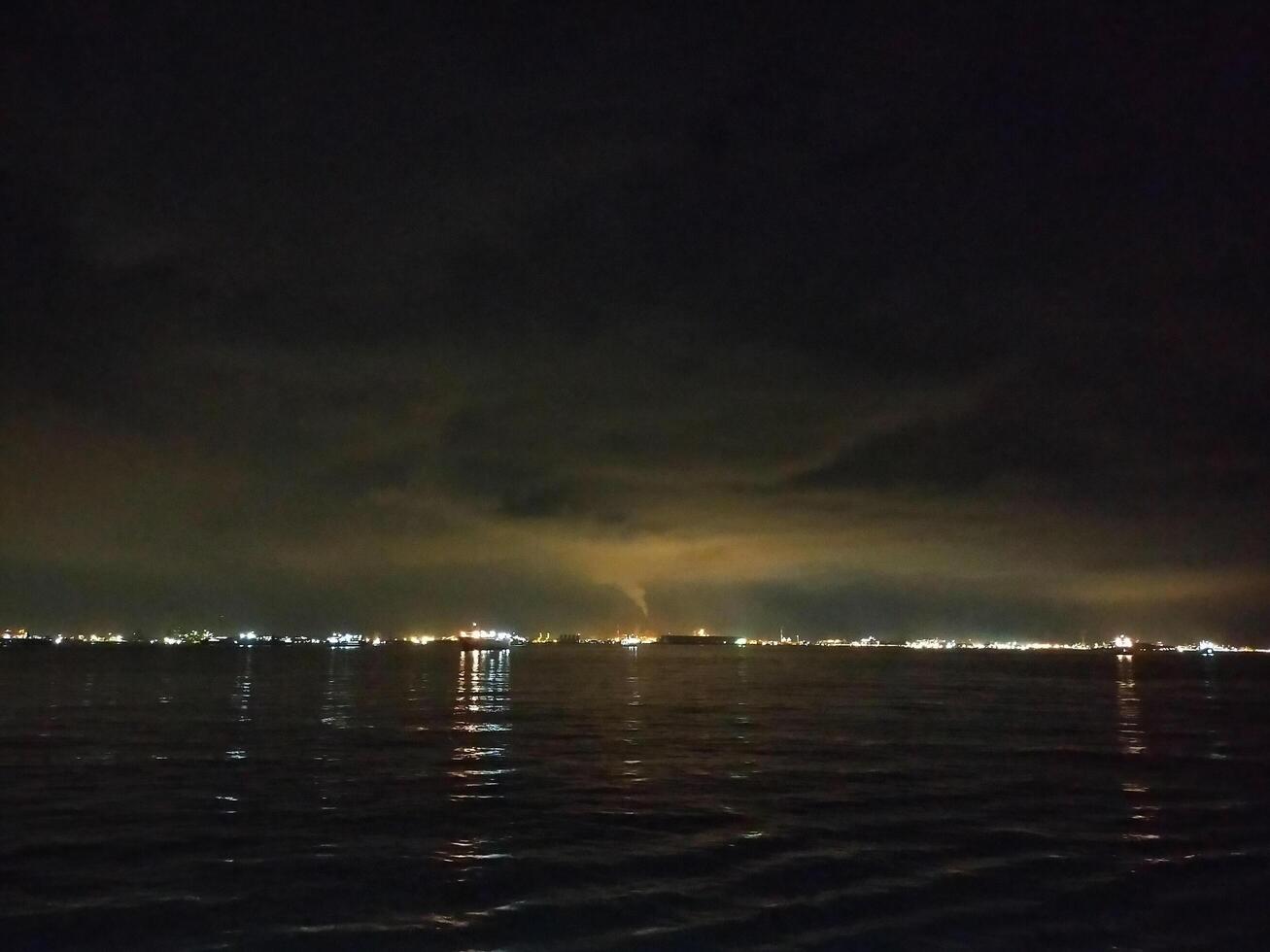 A dark sky over the water with a light coming from the sky photo