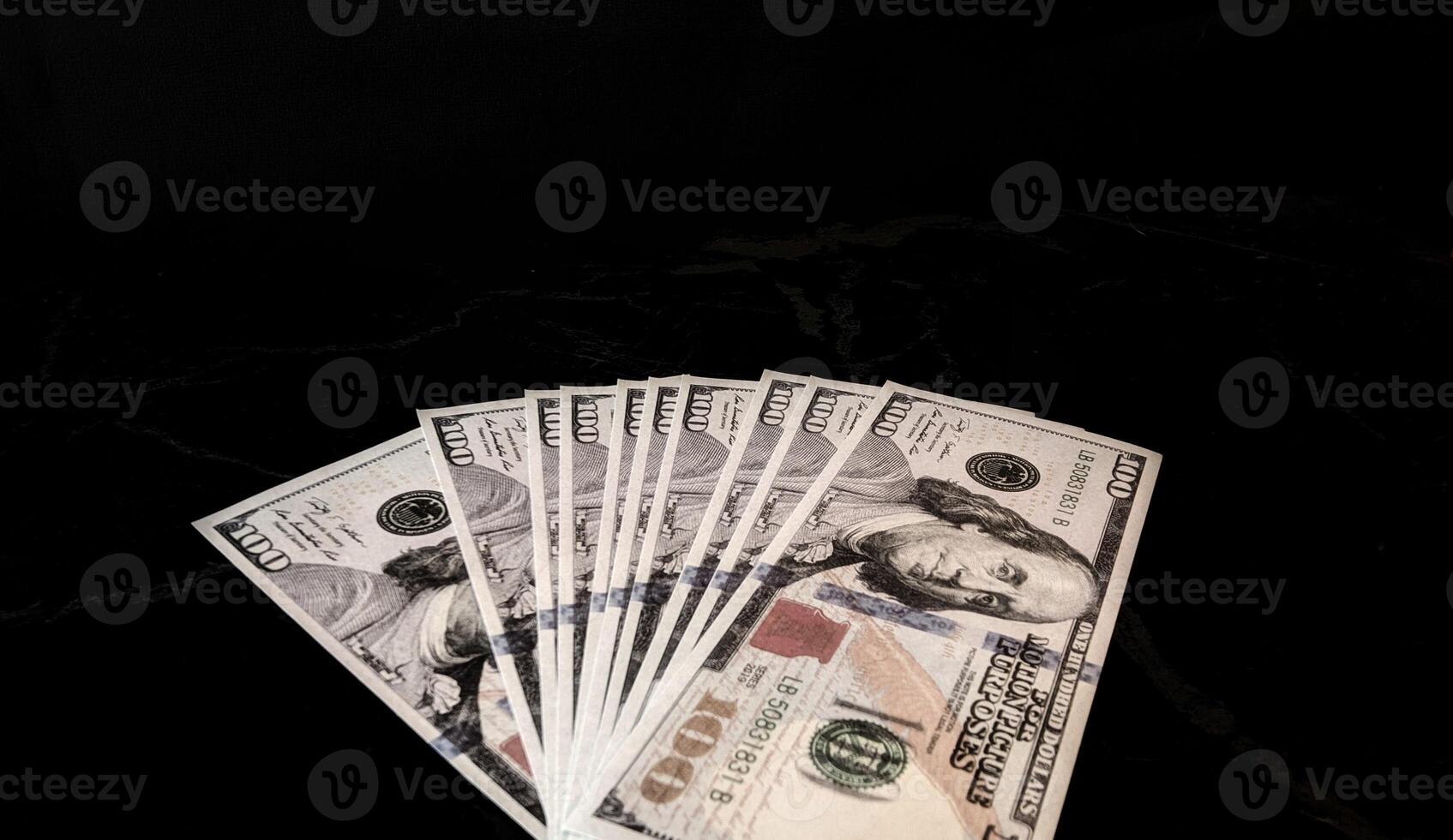A stack of one hundred dollar bills on a black surface photo