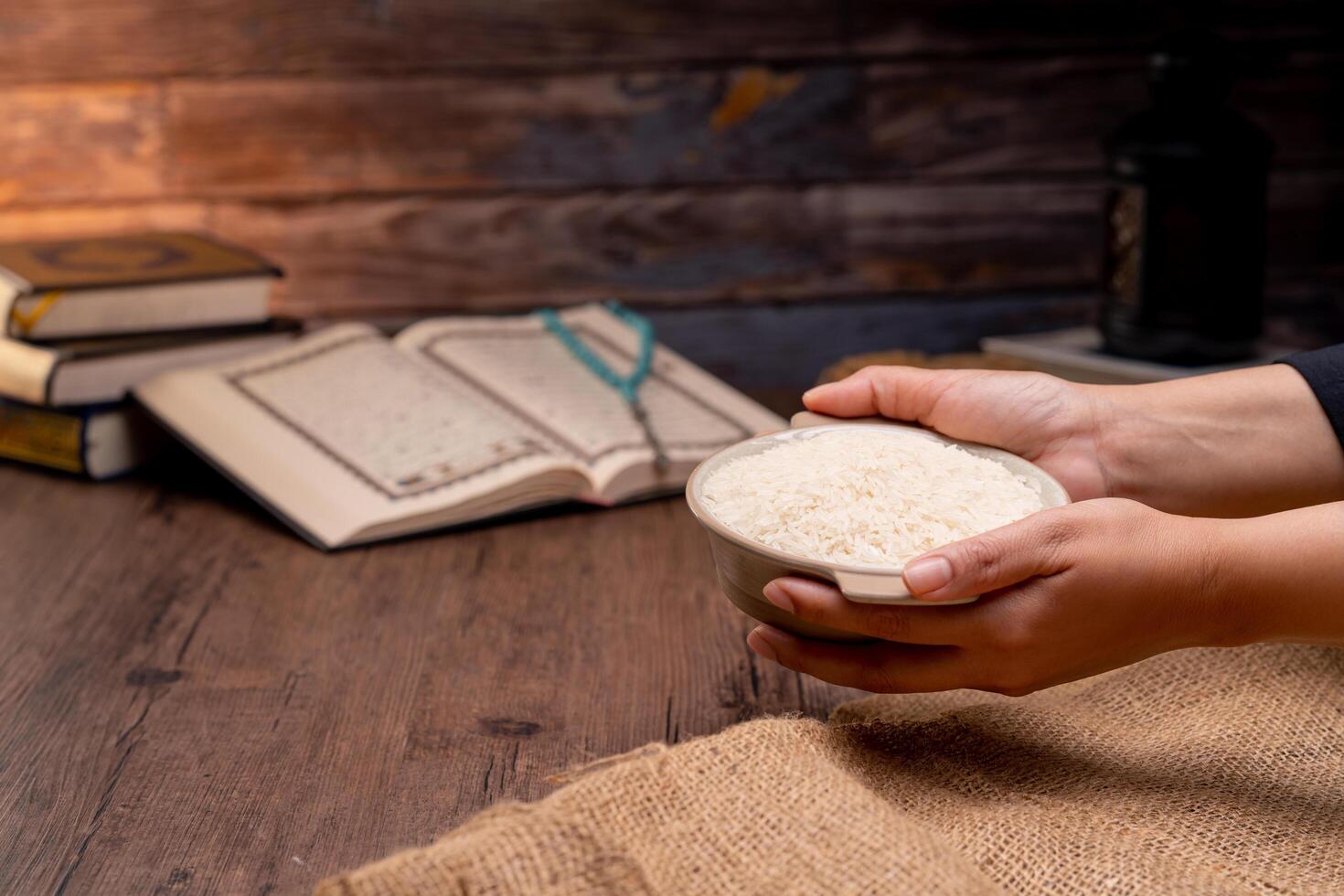 Holy Quran and a grain of rice in a wooden bowl in the sack on a wooden table, Islamic zakat concept. Muslims to help the poor and needy. Conceptual shoot for property, income, and fitrah zakat. photo