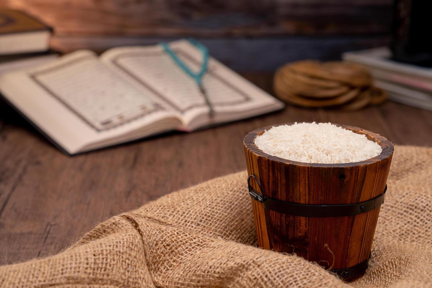 Holy Quran and a grain of rice in a wooden bowl in the sack on a wooden table, Islamic zakat concept. Muslims to help the poor and needy. Conceptual shoot for property, income, and fitrah zakat. photo