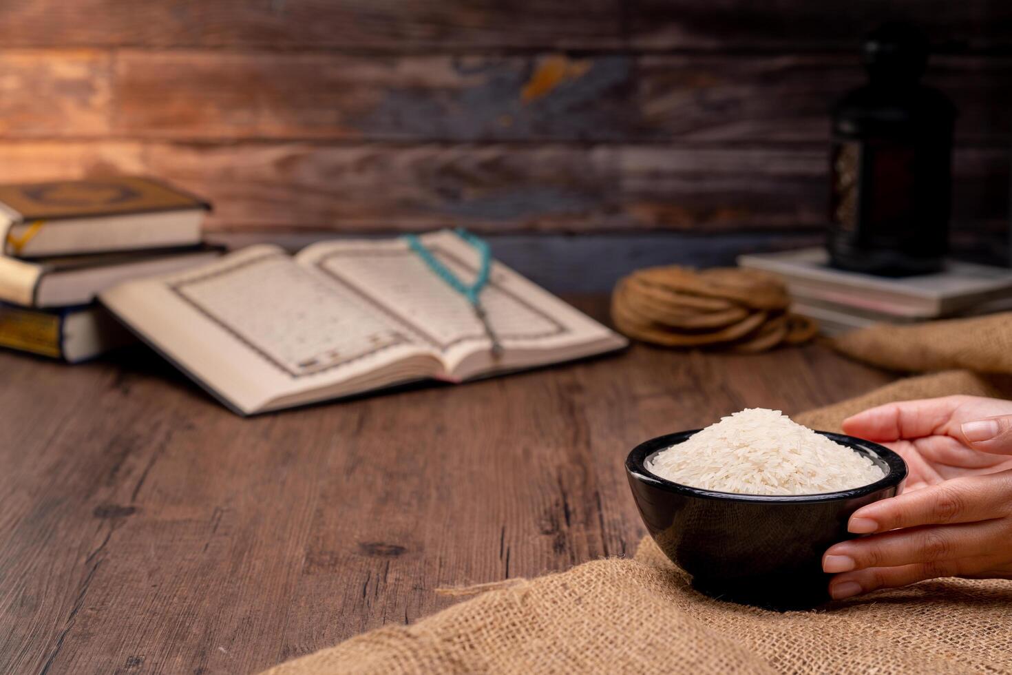 Holy Quran and a grain of rice in a wooden bowl in the sack on a wooden table, Islamic zakat concept. Muslims to help the poor and needy. Conceptual shoot for property, income, and fitrah zakat. photo