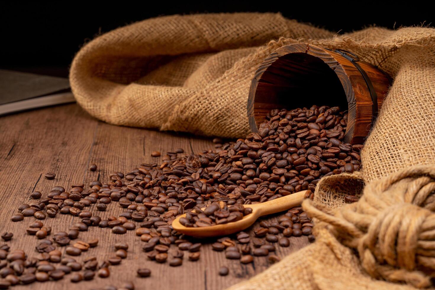 The picture of coffee beans stacked together on a wooden floor in a warm, light atmosphere, on a dark background, with copy space. photo