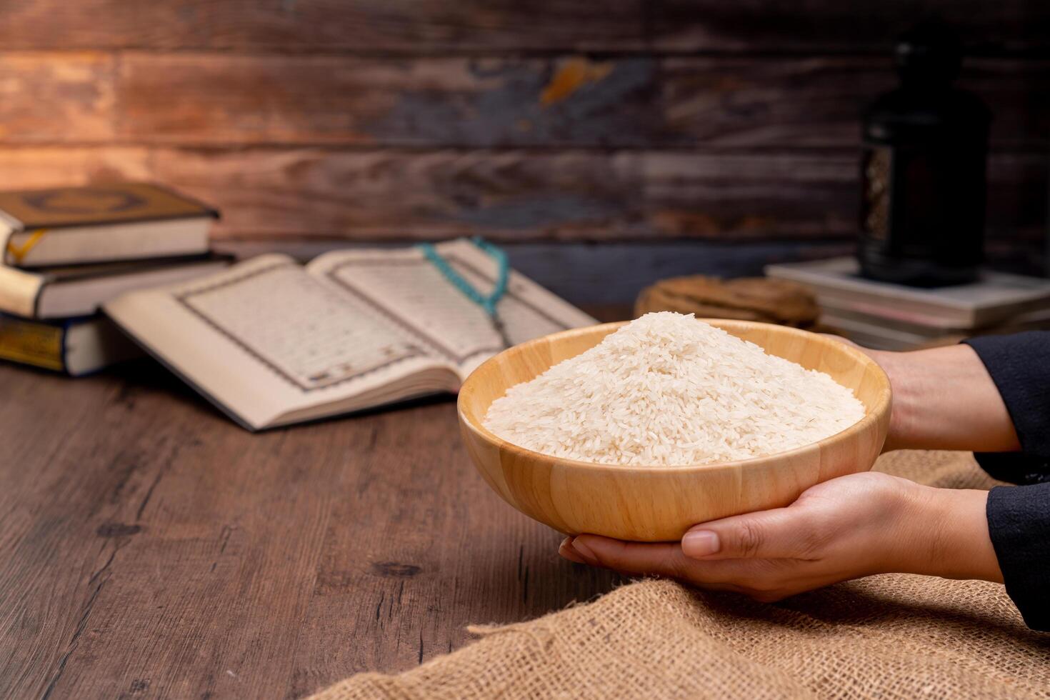 Holy Quran and a grain of rice in a wooden bowl in the sack on a wooden table, Islamic zakat concept. Muslims to help the poor and needy. Conceptual shoot for property, income, and fitrah zakat. photo