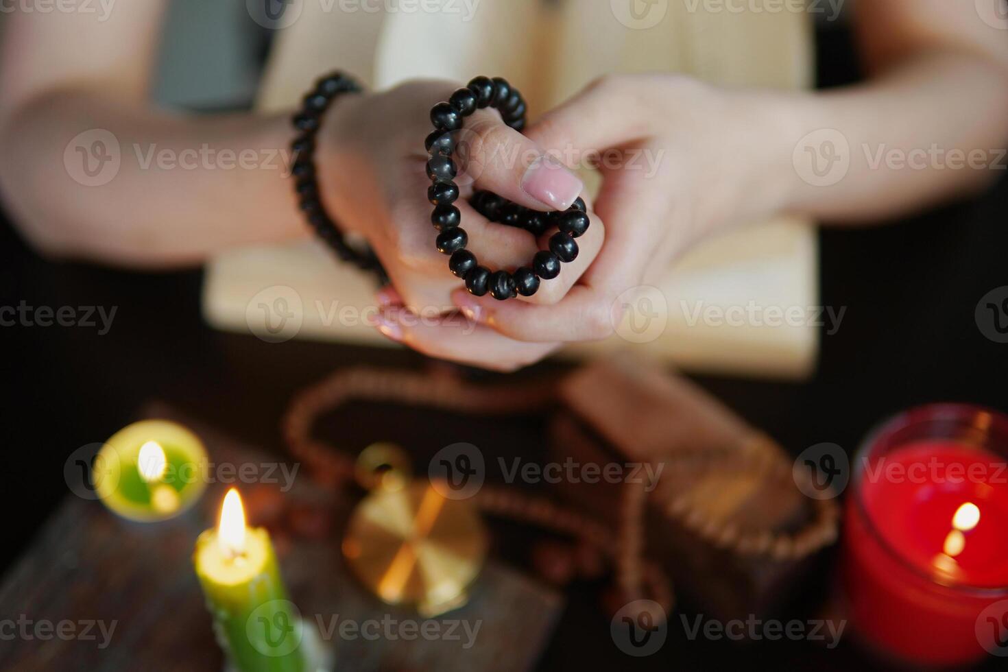 Woman Pray Carrying a rosary necklace on hand near black wooden table with open Bible, she sitting next to a burning candle in room.selective focus. photo