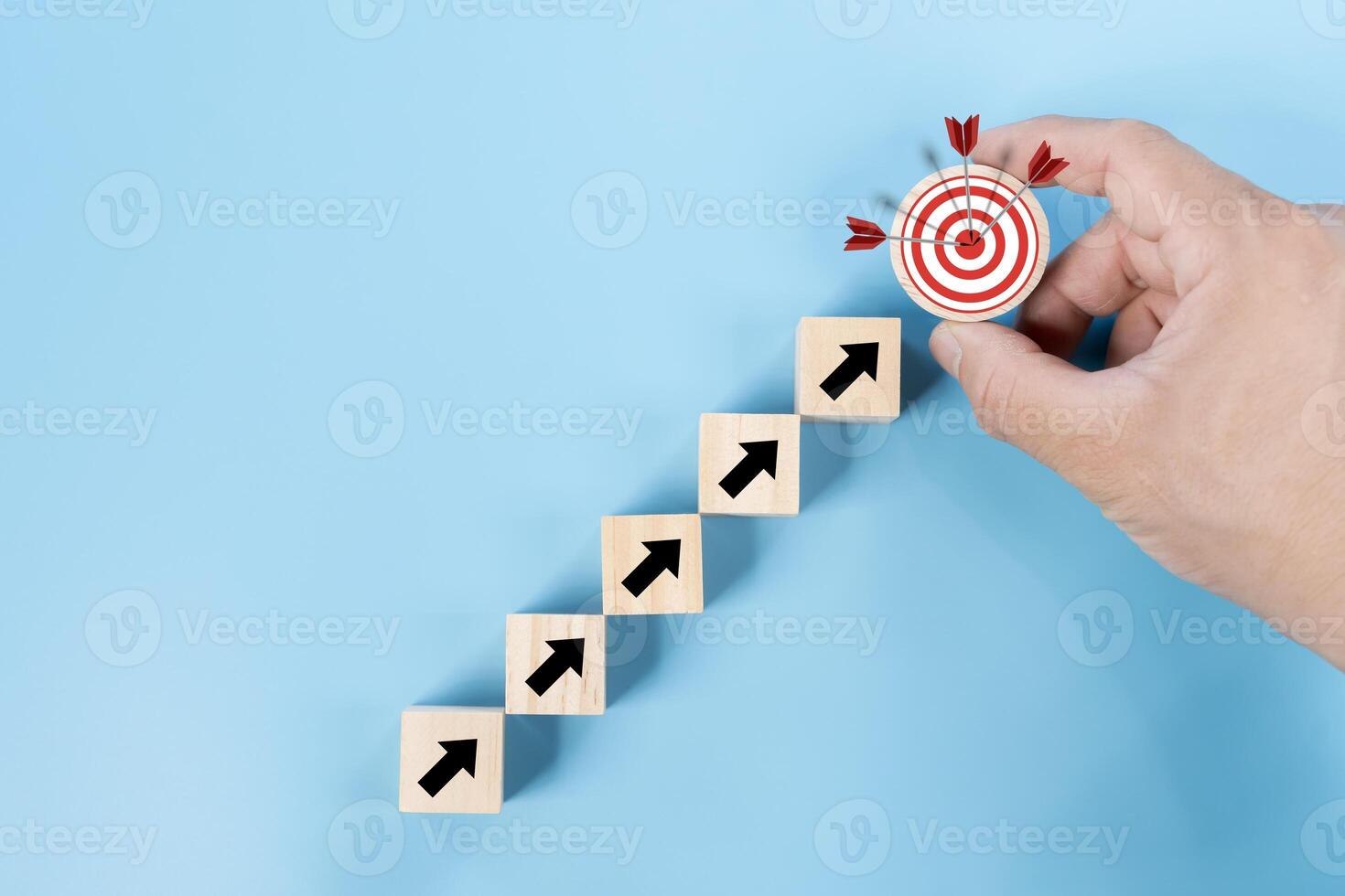 Man hand holding wooden block with target aiming dart board and arrow up on blue background. photo