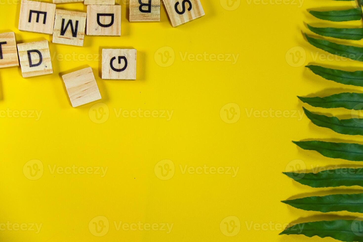 yellow background with green tropical plant branch and wooden alphabet photo
