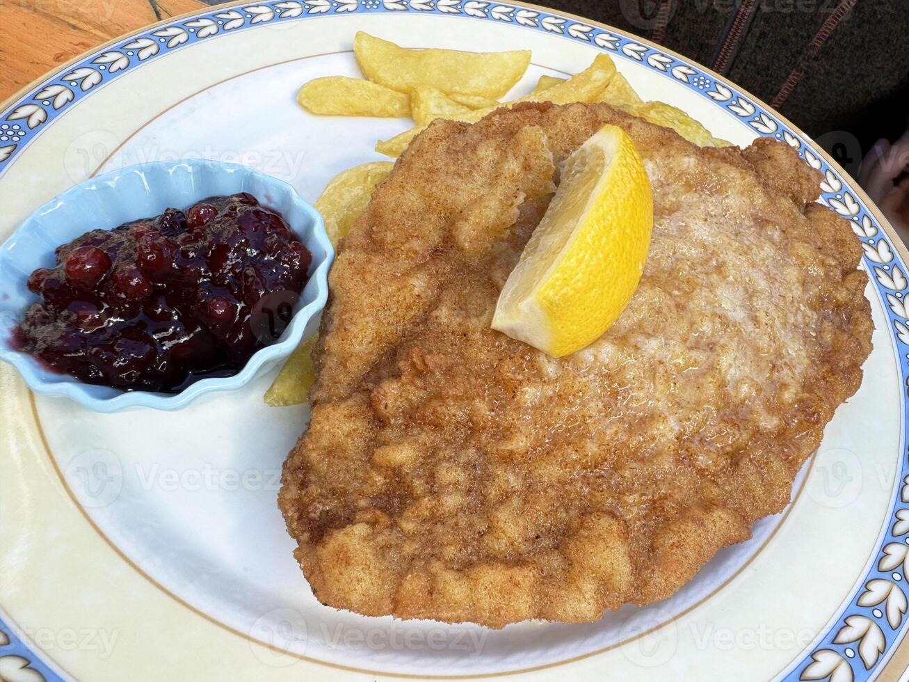 Traditional wiener schnitzel with lemon, fries, and lingonberry sauce on decorative plate photo