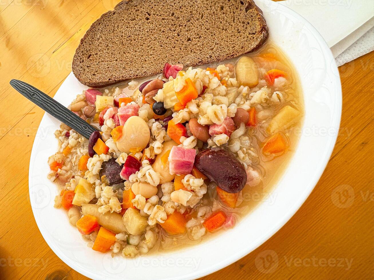 Hearty barley and bean soup with rustic bread on wooden table photo