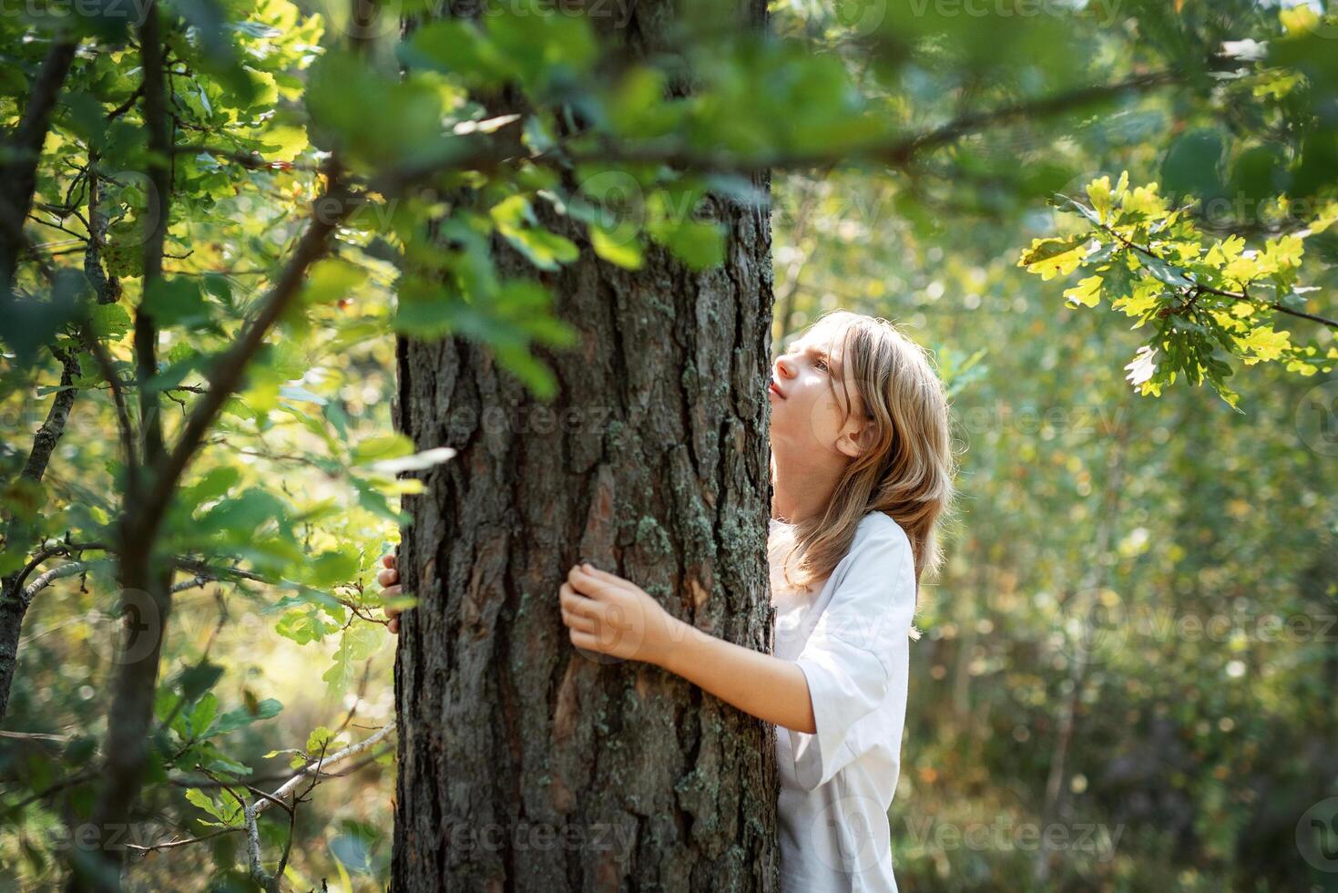 A teenage girl hugs a tree in the forest. photo