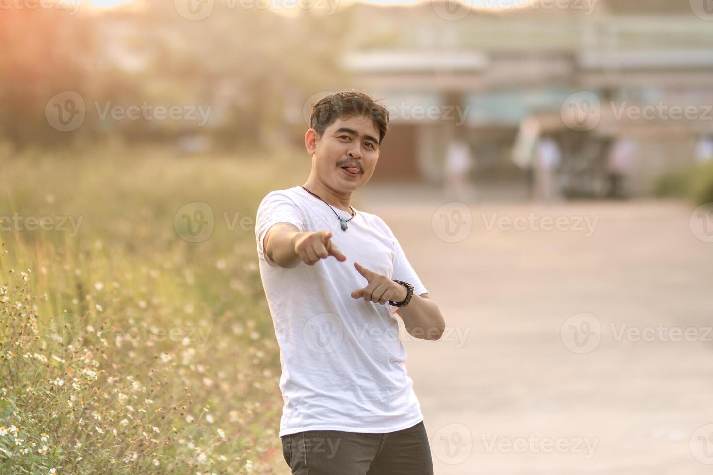 a man standing and smiling. the man points at the camera in the sunny afternoon. photo