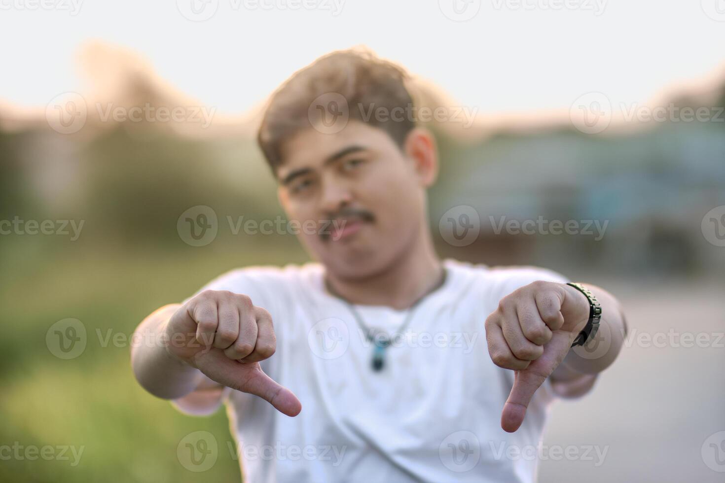 a man standing with a thumbs down. The man acted like someone was underestimating something. set in nature on a sunny afternoon. photo