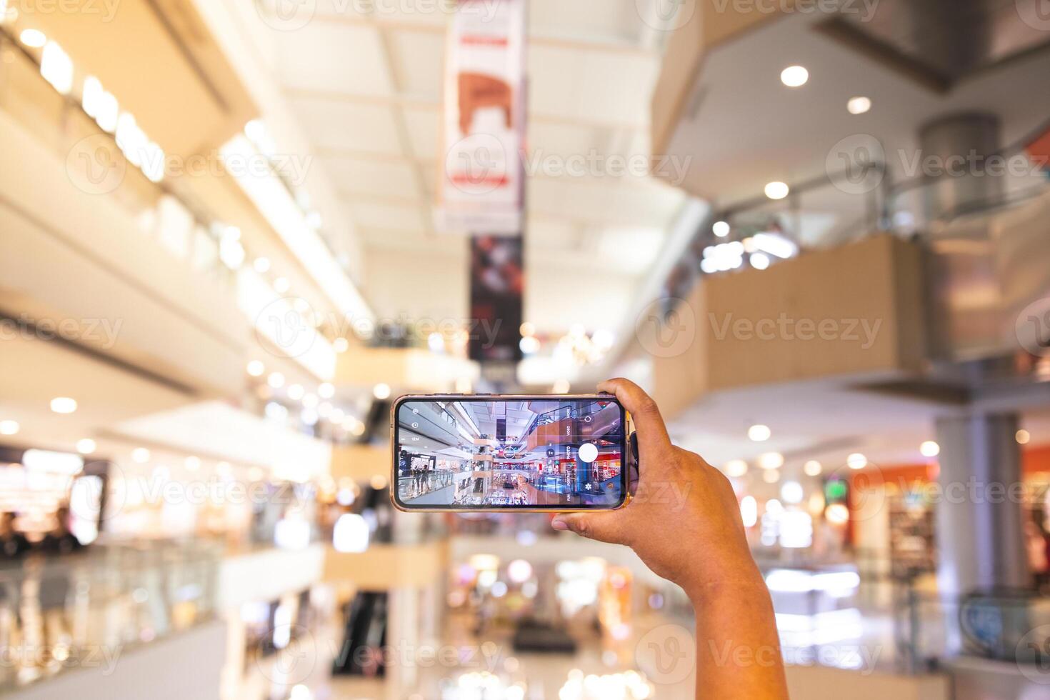 a man's hand taking pictures of objects in the mall. the man is seen using his cellphone to take pictures of objects around him. the portrait results are very clear and good. photo