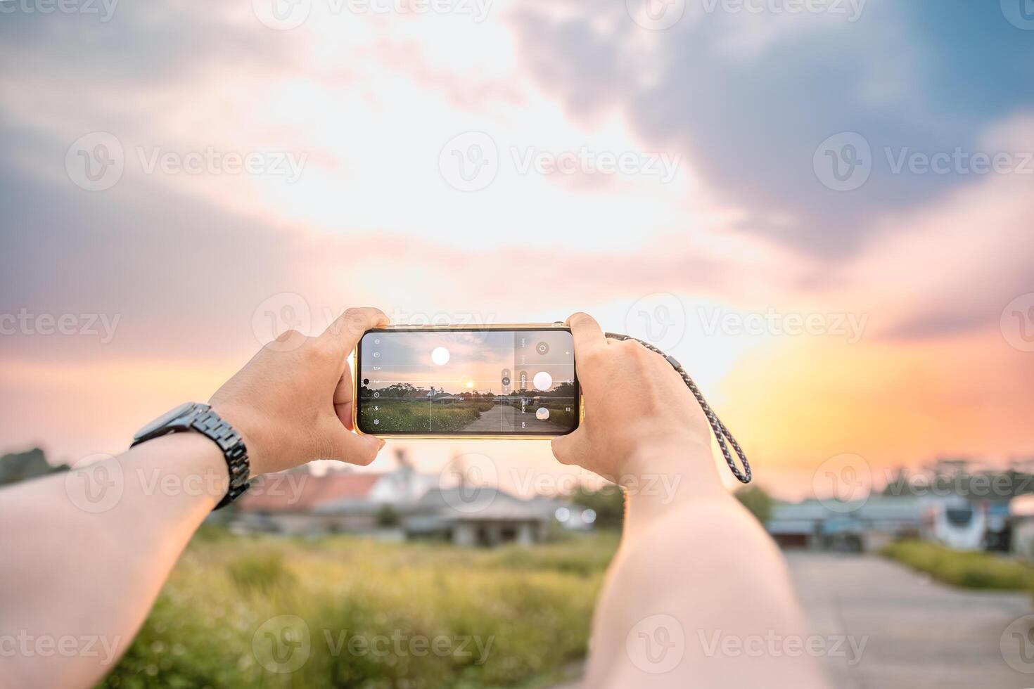 a man who is taking photos of the scenery. he uses a cell phone camera. set in a bright natural atmosphere in the afternoon.