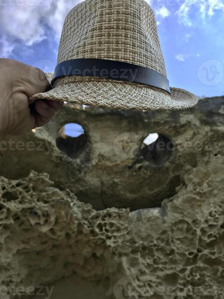 Tourist holds sun hat over Natural rock in form of flying demon. Smiling bat. Bakla, Crimea. photo
