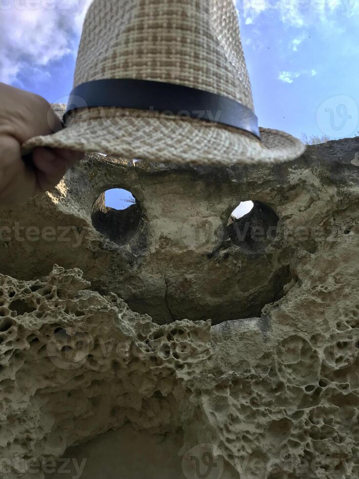 Tourist holds sun hat over Natural rock in form of flying demon. Smiling bat. Bakla, Crimea. photo