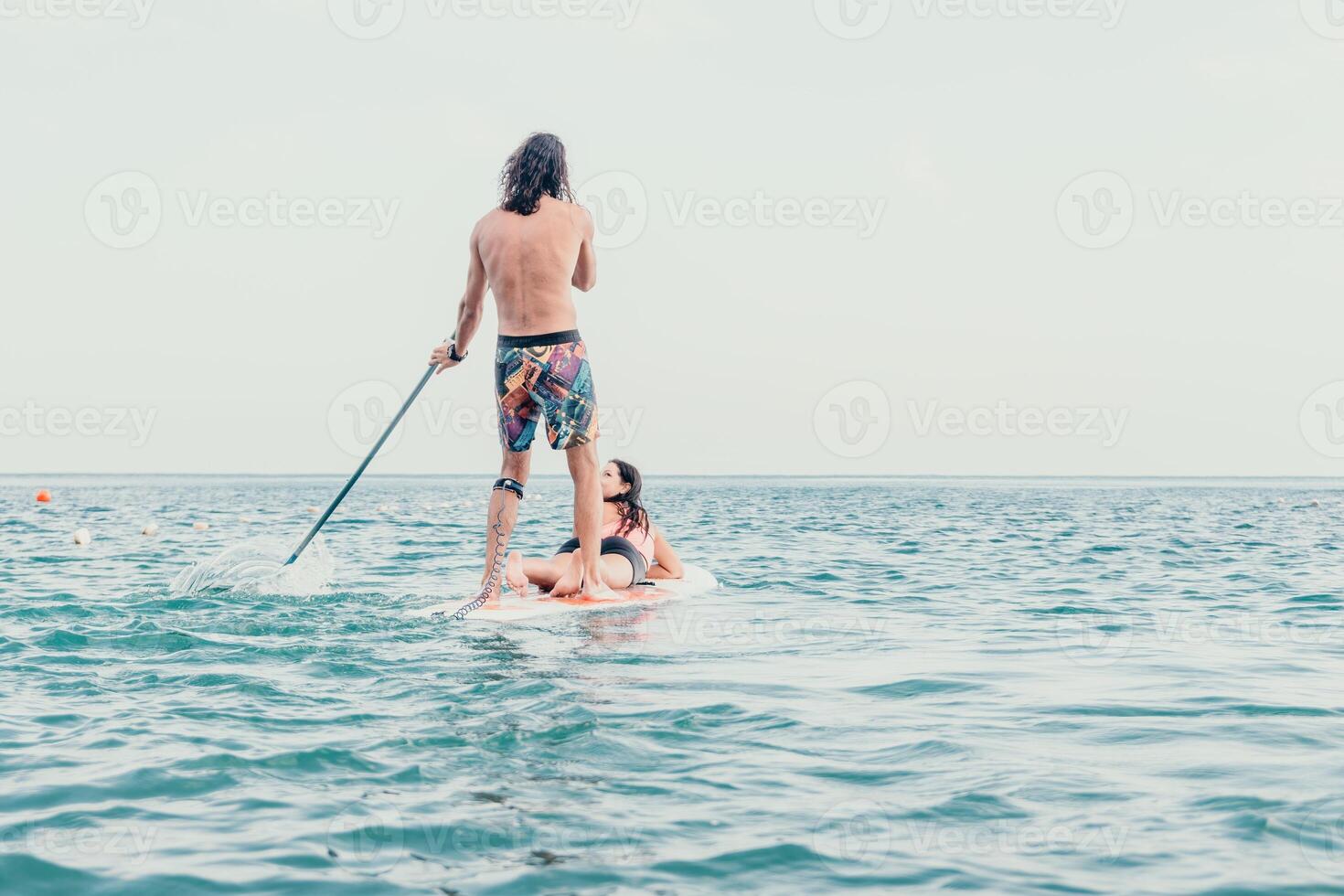 Sea woman and man on sup. Silhouette of happy young woman and man, surfing on SUP board, confident paddling through water surface. Idyllic sunset. Active lifestyle at sea or river. photo