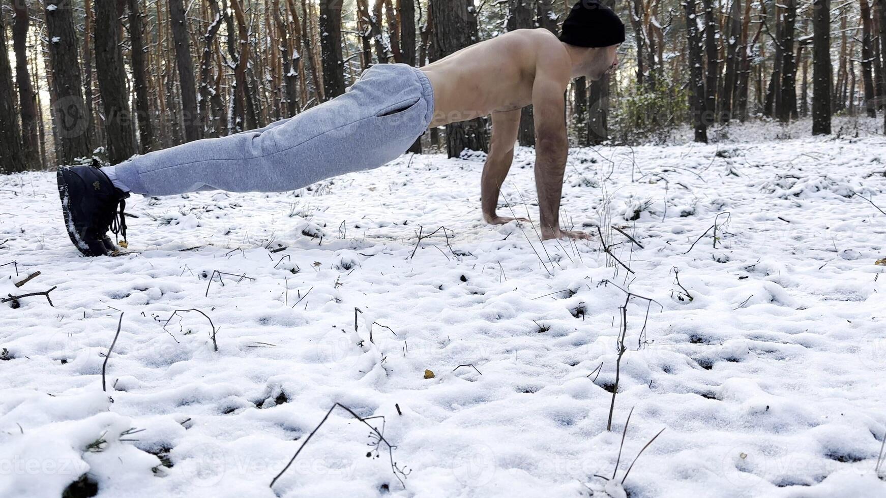Strong man doing push ups on snow at winter forest. Sportsman exercising at nature. Young guy training outdoor. Muscular athlete showing hard and intense workout. Concept of sportive lifestyle photo