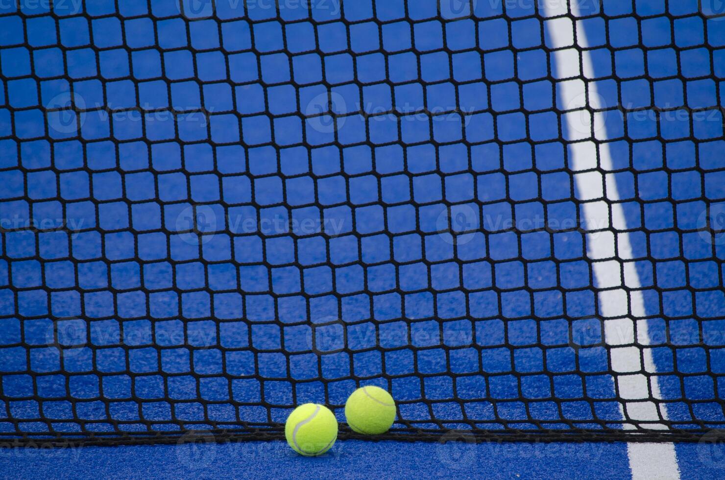 Blue paddle tennis court, two balls next to the net and the line photo