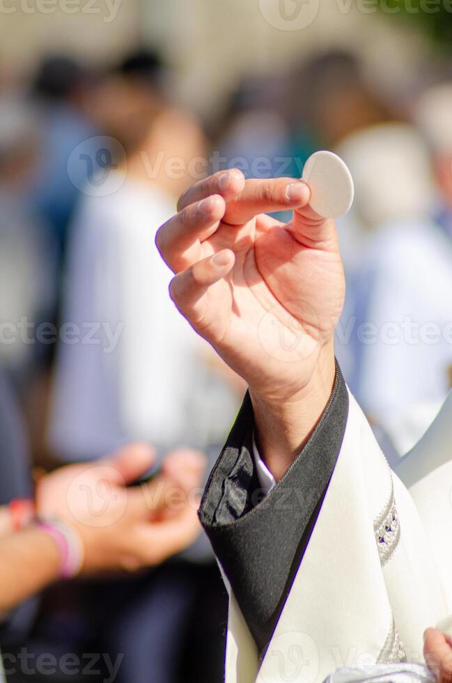 hand of a catholic priest elevating the host in the sacrament of communion at an outdoor service photo