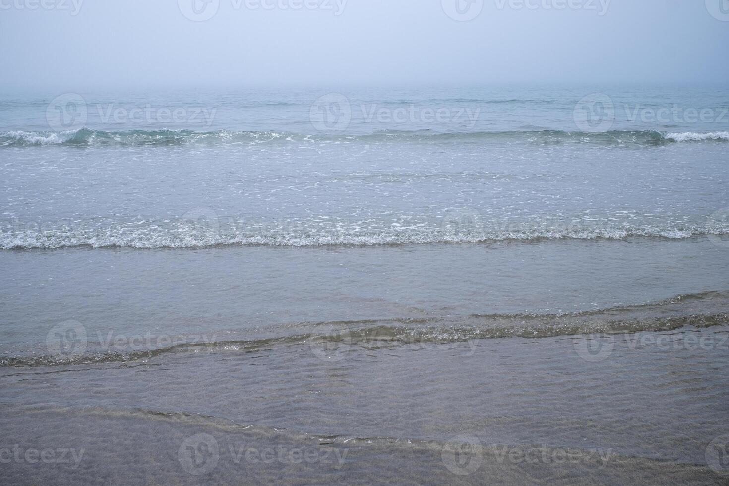 View of the shore of a beach with smooth waves on a cloudy day. photo
