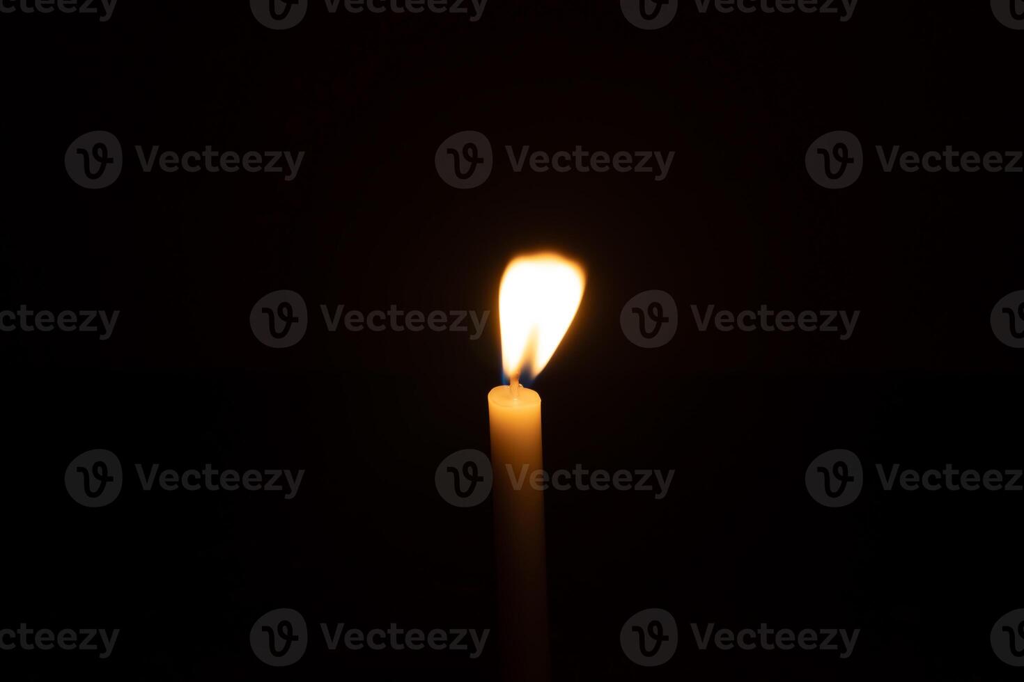 A single burning candle flame or light glowing on a small orange candle on black or dark background on table in church for Christmas, funeral or memorial service with copy space photo