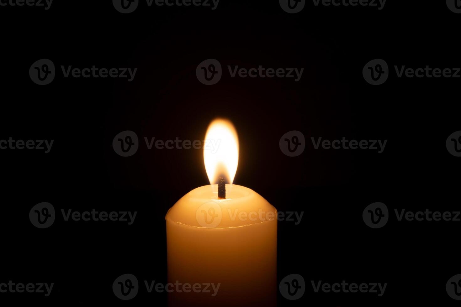 A single burning candle flame or light glowing on a big white candle isolated on red or dark background on table in church for Christmas, funeral or memorial service photo