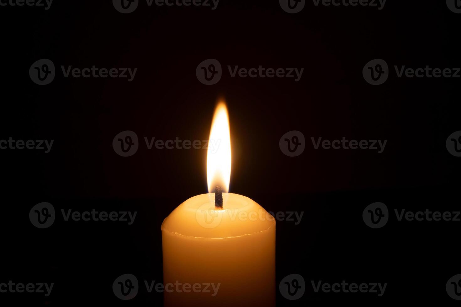 A single burning candle flame or light glowing on a big white candle isolated on red or dark background on table in church for Christmas, funeral or memorial service photo