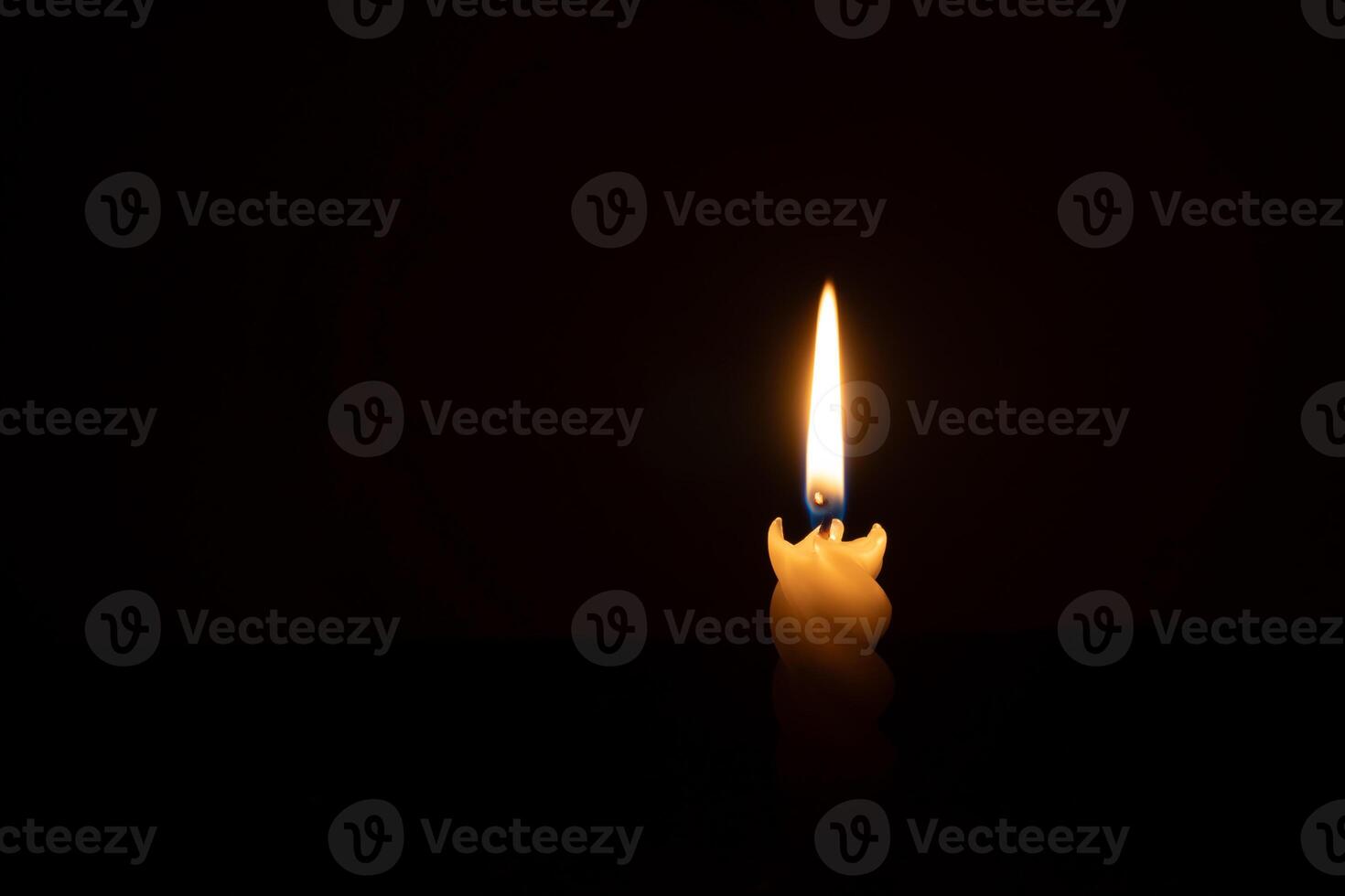 A single burning candle flame or light glowing on a spiral white candle on black or dark background on table in church for Christmas, funeral or memorial service with copy space photo