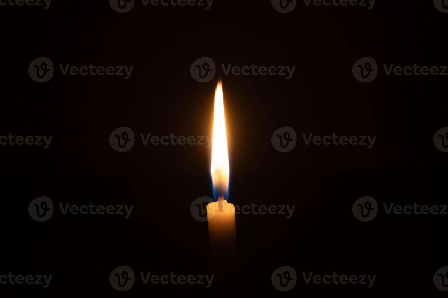 A single burning candle flame or light glowing on a small orange candle on black or dark background on table in church for Christmas, funeral or memorial service with copy space photo