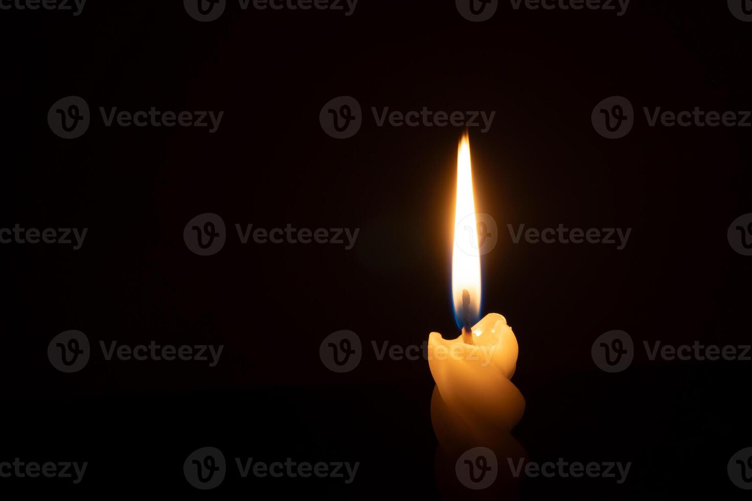 A single burning candle flame or light glowing on a spiral white candle on black or dark background on table in church for Christmas, funeral or memorial service with copy space photo