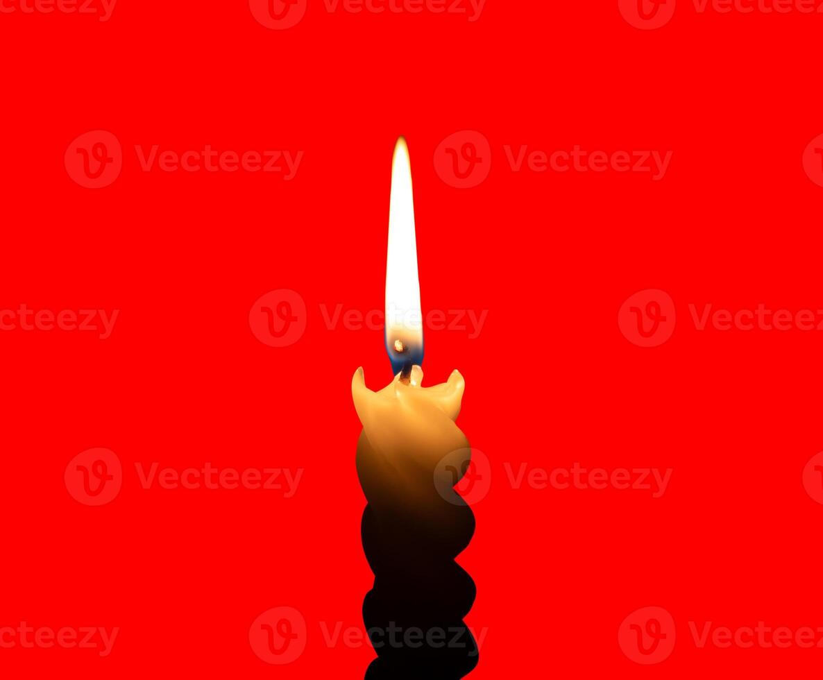 A single burning candle flame or light glowing on a small spiral white candle isolated on red background with clipping path photo