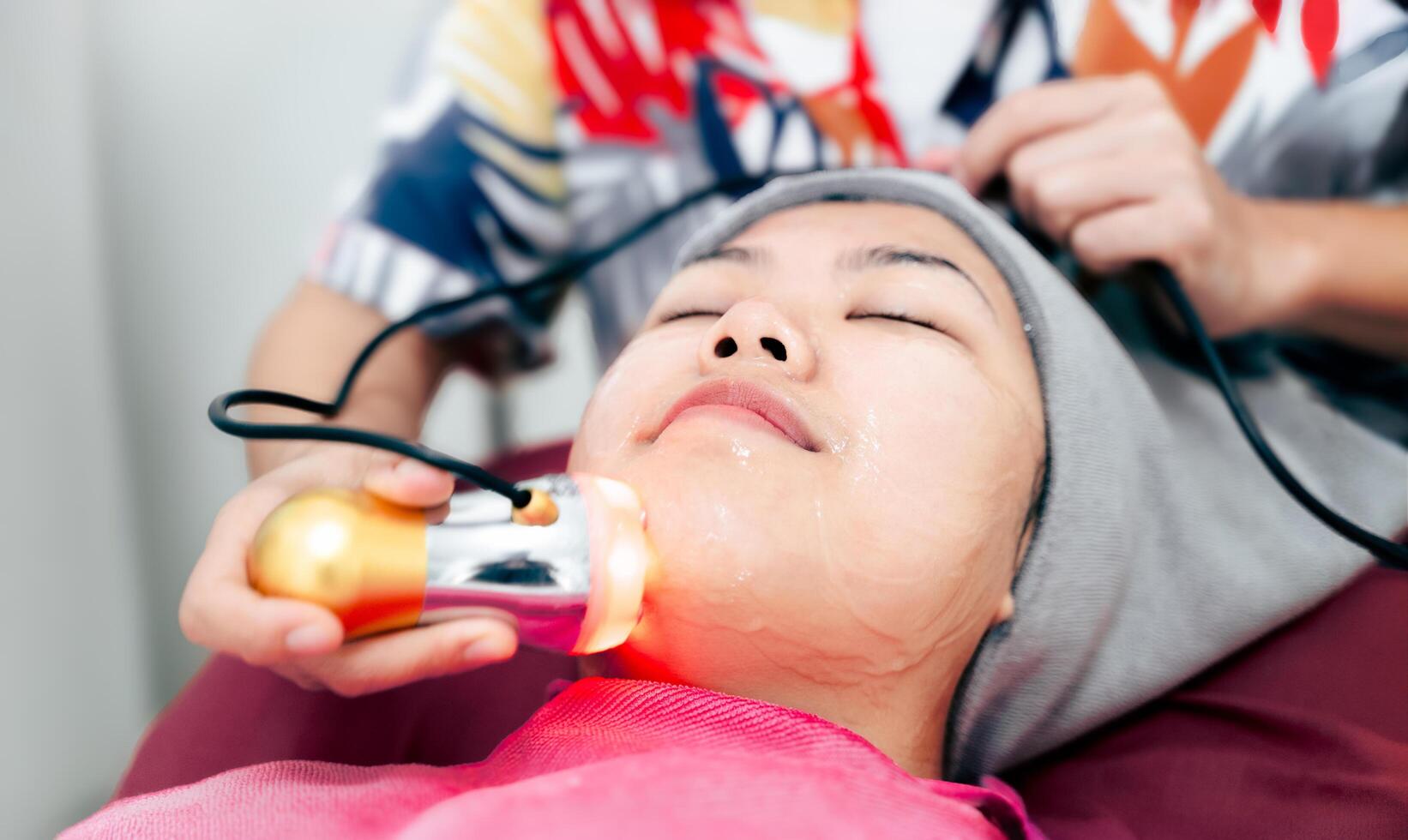 A woman is getting a facial treatment with a device that is emitting a light photo