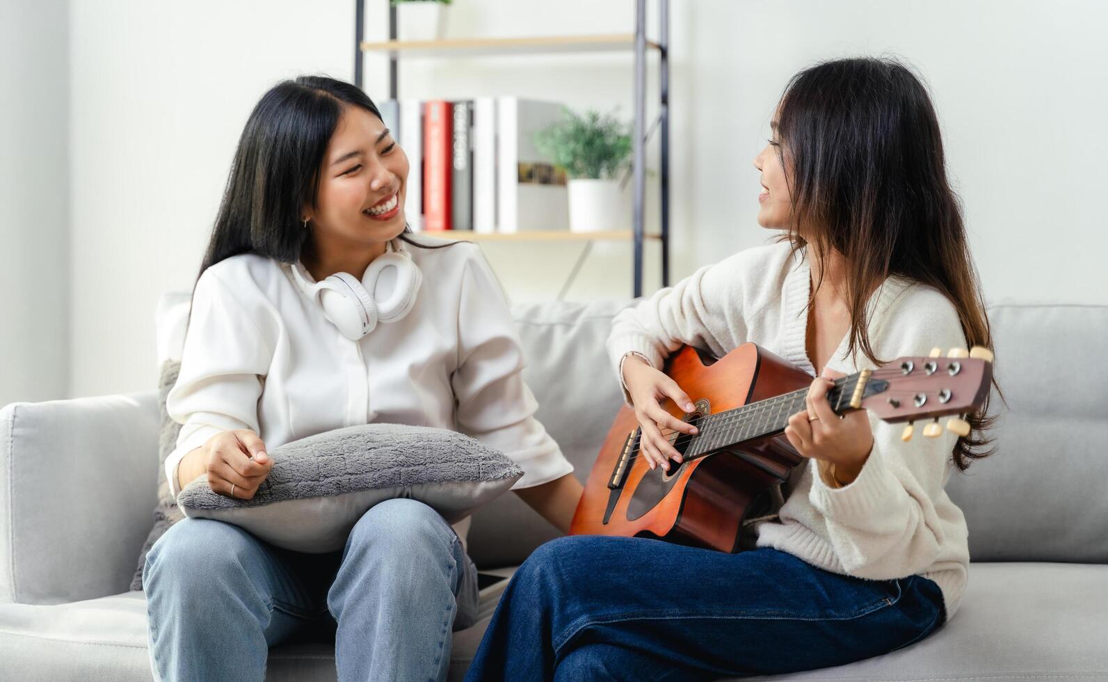 Two women are sitting on a couch, one of them playing a guitar photo
