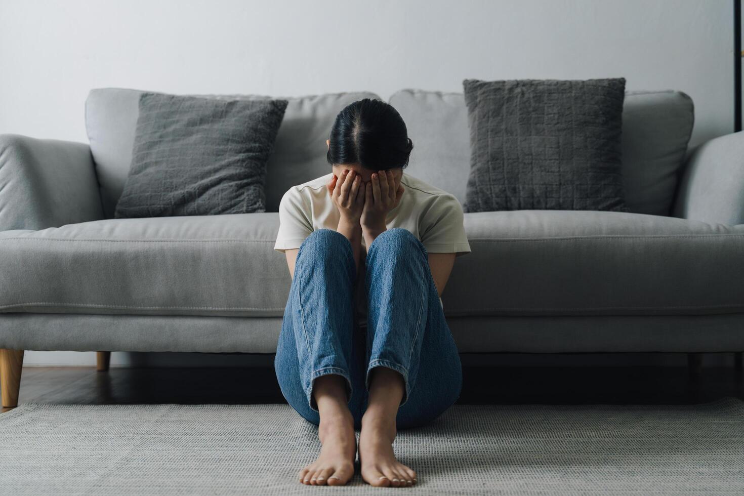 A woman is sitting on the floor in a living room. She is crying and she is in a state of distress photo