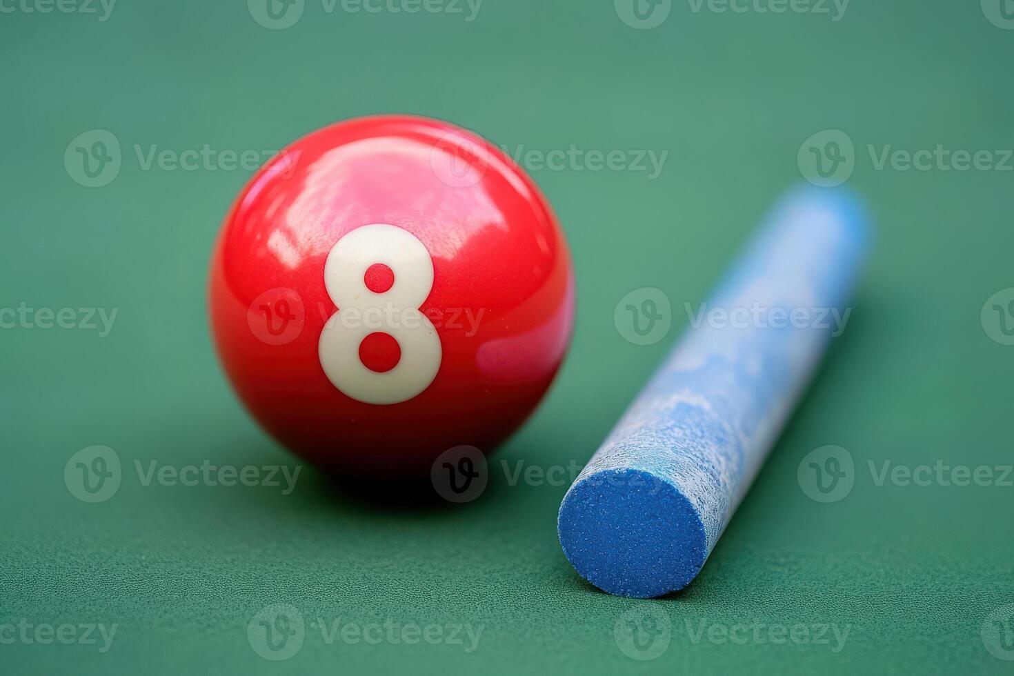 A vibrant red snooker ball marked with the number 8 rests next to a blue chalk stick on a smooth green felt surface. photo